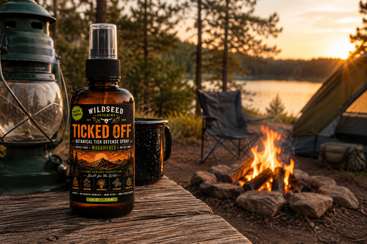 Ticked Off natural botanical tick and mosquito spray bottle on a camping table beside a campfire at sunset